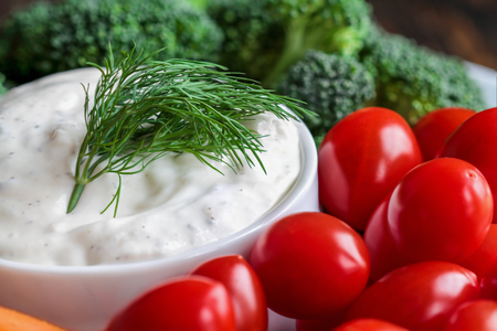 Homemade buttermilk ranch salad dressing with dill served with cherry tomatoes, baby carrots and broccoli, over a rustic wooden background.の写真素材