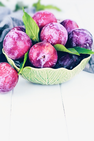 Freshly picked homegrown organic plums from the tree with leaves in a bowl.の写真素材