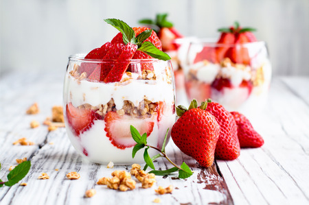 Healthy breakfast of strawberry parfaits made with fresh fruit, yogurt and granola over a rustic white table. Shallow depth of field with selective focus on glass jar in front. Blurred background.の写真素材