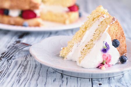 Slice of Victoria Sponge Cake with whipped cream, sugared flower petals and fresh berries over a...