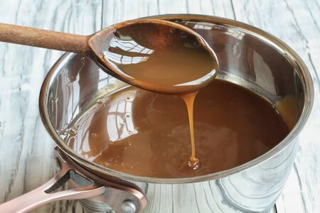 Wooden spoon dripping caramel sauce into a pan. Selective focus with blurred background.の写真素材