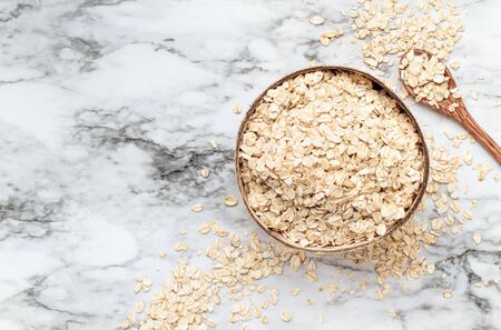 Healthy raw uncooked quick oat flakes in a wooden bowl over a marble table background. Shot from top...