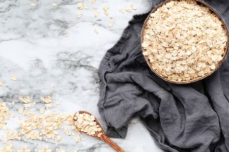 Healthy raw uncooked quick oat flakes in a wooden bowl over a marble table background. Shot from top view.の写真素材