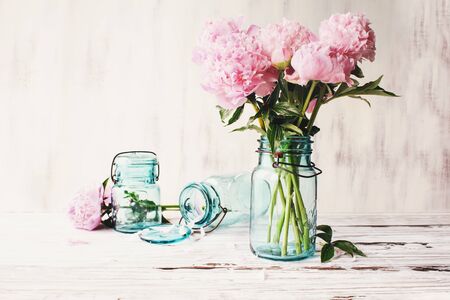 Beautiful pink Peony flowers in an antique blue mason jar over a white rustic wood table background  with copy space for your text. Image edited to give farmhouse decor style.の写真素材
