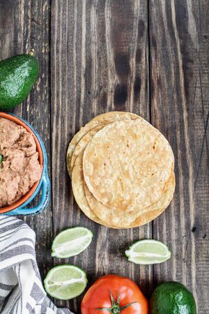 Ingredients of fried corn tortillas, refried beans, avocados, tomatoes and fresh limes for making vegan Tostadas. Top view, flatlay.の写真素材