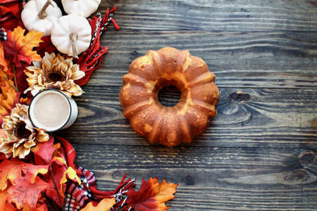Delicious, naked pumpkin spice bundt cake with Autumn leaves and coffee over a rustic woode table background. Image shot from top view..の写真素材