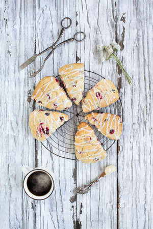 Traditional fresh baked English cranberry or cherry tea scones over rustic background with a hot cup...