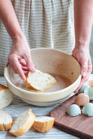 Woman's hands dipping bread into French toast batter with farm fresh organic eggs and a loaf of...