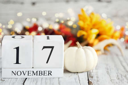 White wood calendar blocks with the date November 17th and autumn decorations over a wooden table. Selective focus with blurred background.の写真素材