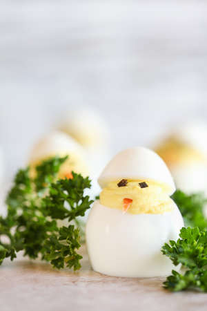 Deviled eggs for Easter decorated as cute little chicks hatching from eggs with carrot beak and...