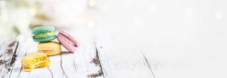Banner with macarons. Bite missing from a lemon french macaron in front over a white rustic table.. Selective focus with blurred background and copy space.の写真素材