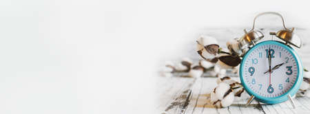 Set your clocks back with this banner of a clock and cotton over a white wooden table. Daylight saving time concept. Selective focus with blurred background.の写真素材