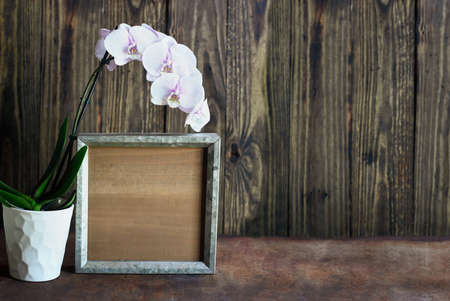 Blank wood farmhouse sign or picture frame with a flowering orchid over a rustic table with wooden...