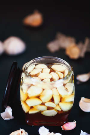 Fermented garlic cloves in a jar of honey, a rich source of probiptics, over a rustic wood background table. Selective focus with blurred background and foreground.の写真素材