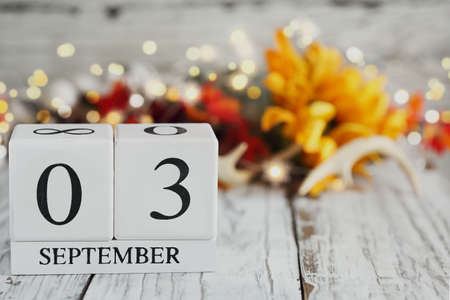 White wood calendar blocks with the date September 3rd and autumn decorations over a wooden table. Selective focus with blurred background.の写真素材