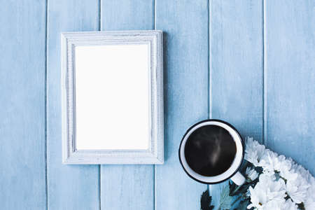 Blank vertical empty picture frame over blue rustic background with steaming coffee and white daisy...