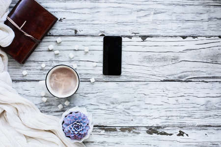 Autumn or winter background shot from top view with hot cocoa, houseplant, cell phone, book, and throw blanket over rustic white wood table. Overhead top view.の写真素材