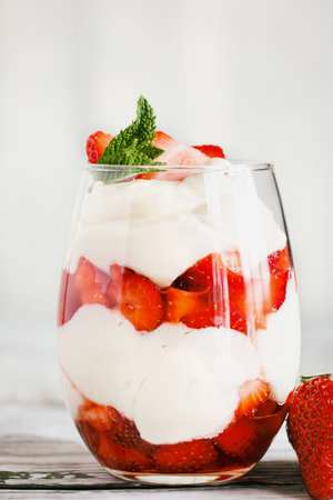 Healthy breakfast of strawberry parfait made with fresh fruit, and yogurt over a rustic white table. Selective focus on glass with blurred background and foreground.