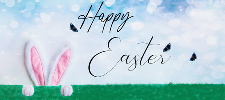 Easter rabbit with cute bunny ears and paws over a pastel blue sky behind a green background with...
