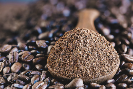 Abstract of a wooden spoonful of ground coffee over a layer of fresh roasted coffee beans. Extreme selective focus on center with blurred foreground and background.の写真素材