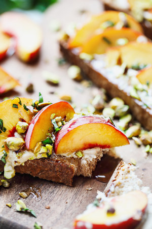 Fresh peach and pistachio whole wheat toast with whipped vegan ricotta cheese, basil and honey. Selective focus with blurred foreground and background.の写真素材