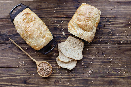 Above table top view of freshly baked whole wheat bread loaves with wooden spoon filled with grain....
