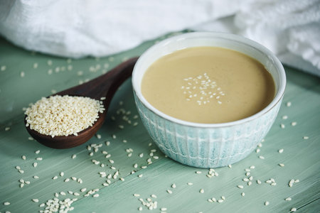 Top view of pretty bowl filled with tahini sauce. Wooden spoon overflowing with sesame seeds. Top view.の写真素材