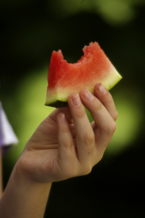 A close up of a girl holding a slice of red watermelon that has a bite out of itの写真素材
