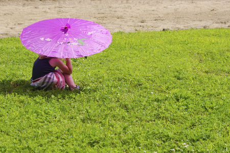 Girl sitting under pink umbrellaの写真素材