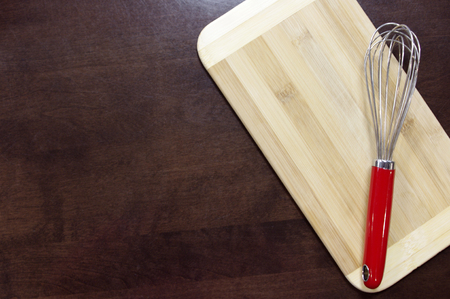 Wisk with red handle on wooden cutting board on dark backgroundの写真素材