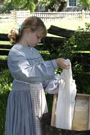 Girl dressed as Pioneer washing laundry outside with washboard in summerの写真素材