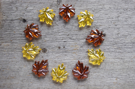 Yellow and orange glass leaves in a circle on rustic wooden background with copy spaceの写真素材