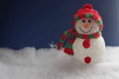 cute snowman ornament on white snow with dark blue background and copy space