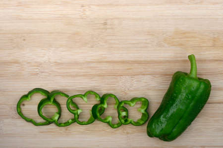 ripe green pepper with ring slices on wooden background with copy spaceの写真素材