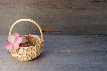small whicker basket with pink hydrangea flower on side on rustic wooden background with copy spaceの写真素材