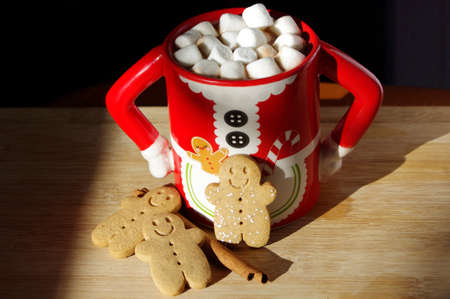 three gingerbread  smiley face cookies in a funny Mrs. Santa Clause coffee mug with hot chocolate, marshmallowsの写真素材
