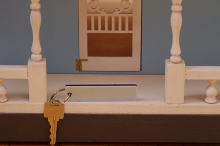 silver key with white tag hanging in front of large blue wooden doll houseの写真素材
