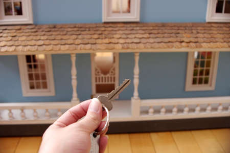 hand holding silver keys with tag in front of large blue wooden doll house