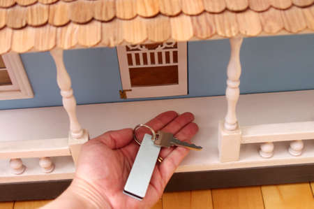 hand holding silver key with white tag on front porch of large blue wooden doll house