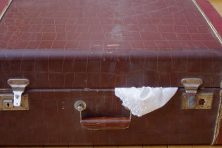 close up of old large vintage brown closed suitcase with lace sticking outの写真素材