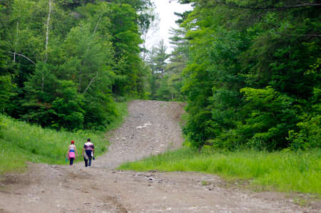 girl and father hiking up dirt and rock tree-lined path in woodsの写真素材