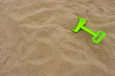 bright green plastic toy shovel on background of brown sand with copy spaceの写真素材