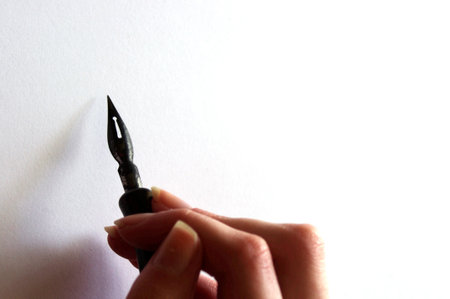 female hand holding a black fountain pen on white paper with copy spaceの写真素材