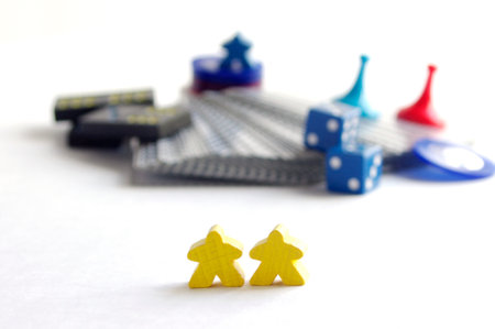 two yellow wooden meeple game pieces in front of blurry game partsの写真素材