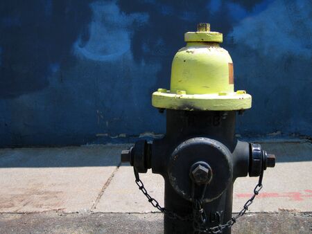 Yellow fire hydrant in front of a bright blue wall with copy spaceの写真素材