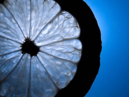 Silhouette of a lemon slice against a bright blue illuminated backgroundの写真素材