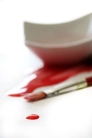 A drop of red paint with paintbrush and spilled paint in backgroundの写真素材