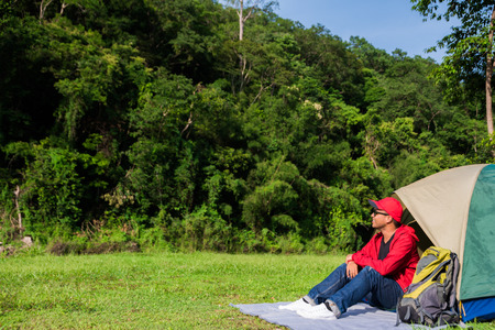 Young asian tourist backpacker sitting in a tent camping in Forest.の写真素材
