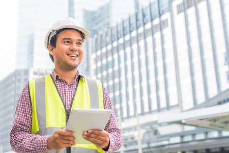 Young handsome asian civil engineer holding tablet looking forward and thinking, planning on...
