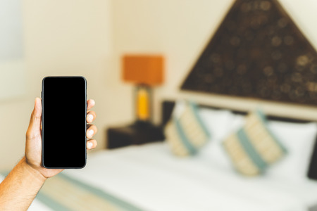 Male hand showing blank space of  smartphone on bedroom hotel background. booking concept.の写真素材